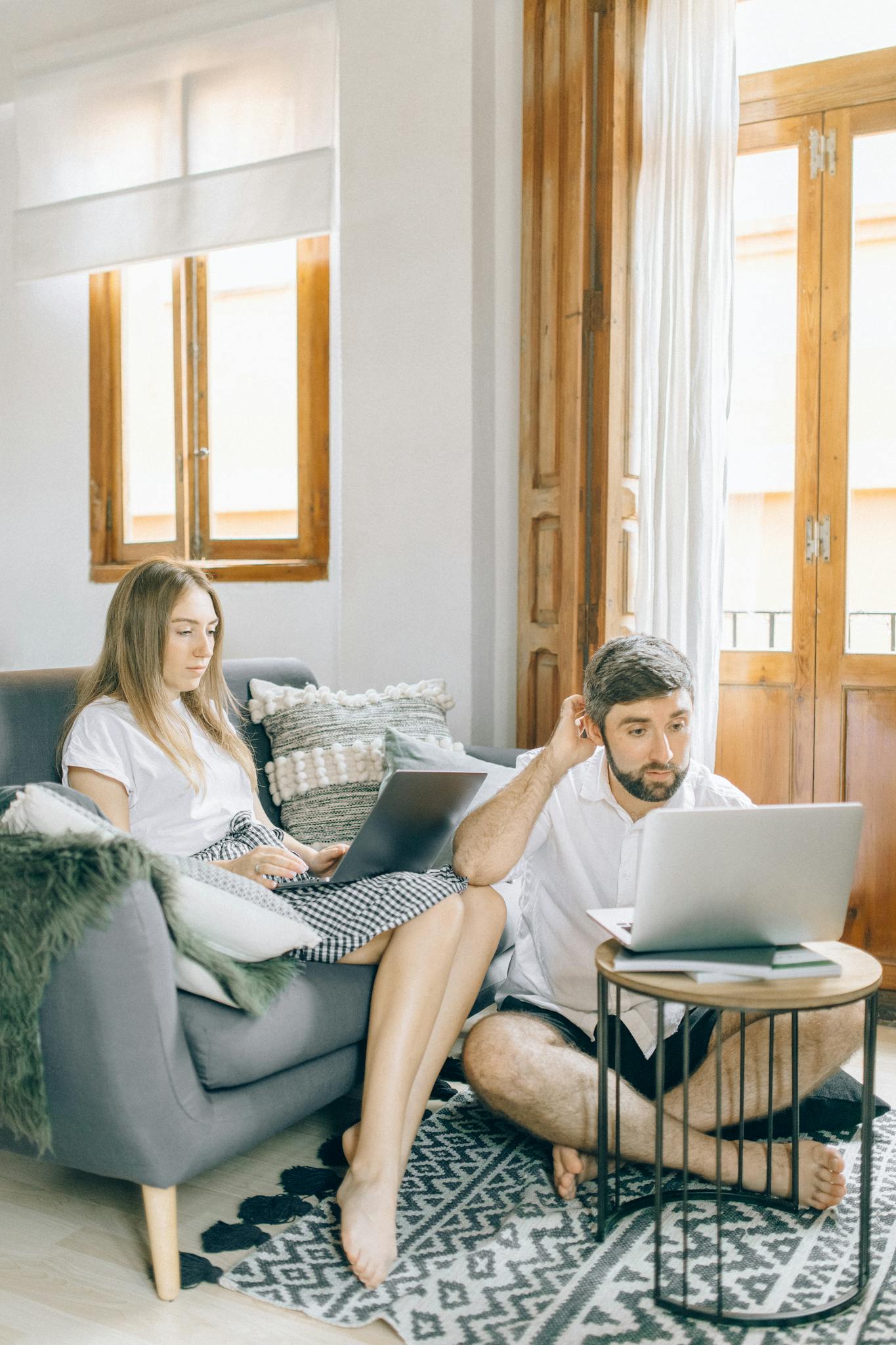 Caucasian couple working from home with laptops, sitting in a bright living room. Cozy and relaxed setting.