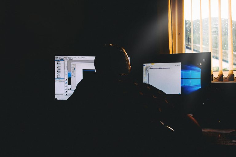 Silhouette of a person working on computers in a dimly lit office environment.